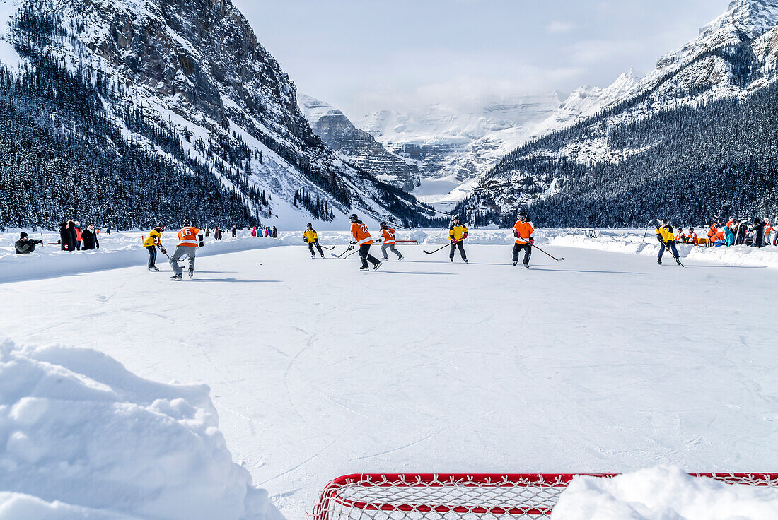 'A pair of hockey teams compete in pond hockey on Lake Louise at the Fairmont Chateau Lake Louise pond hockey tournament in the winter; Lake Louise, Alberta, Canada'
