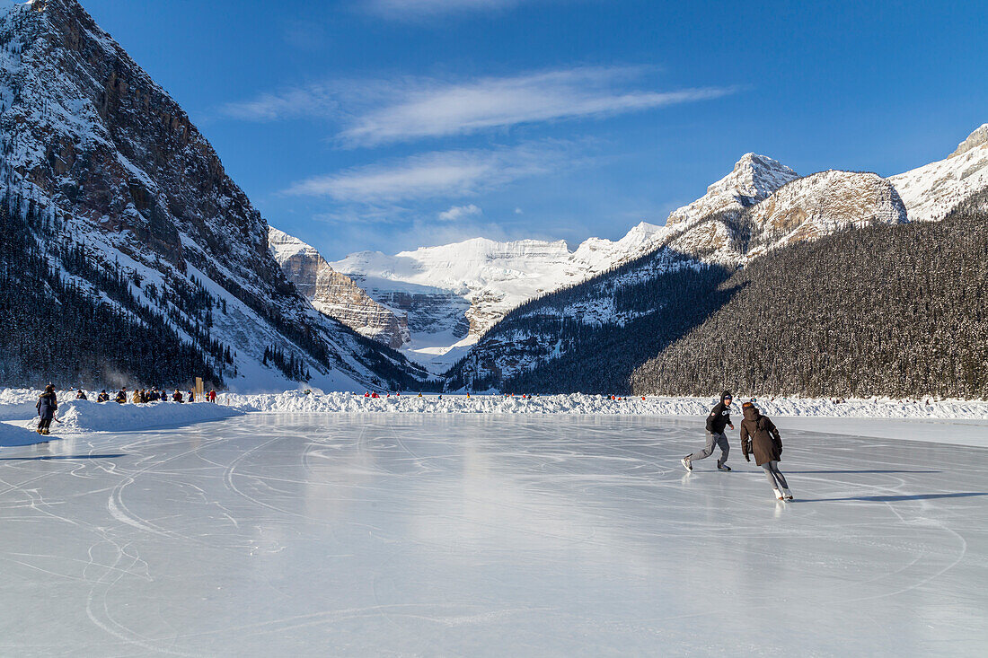 'Tourists enjoy ice skating on the frozen lake on a sunny day with this scenic mountain view; Lake Louise, Alberta, Canada'
