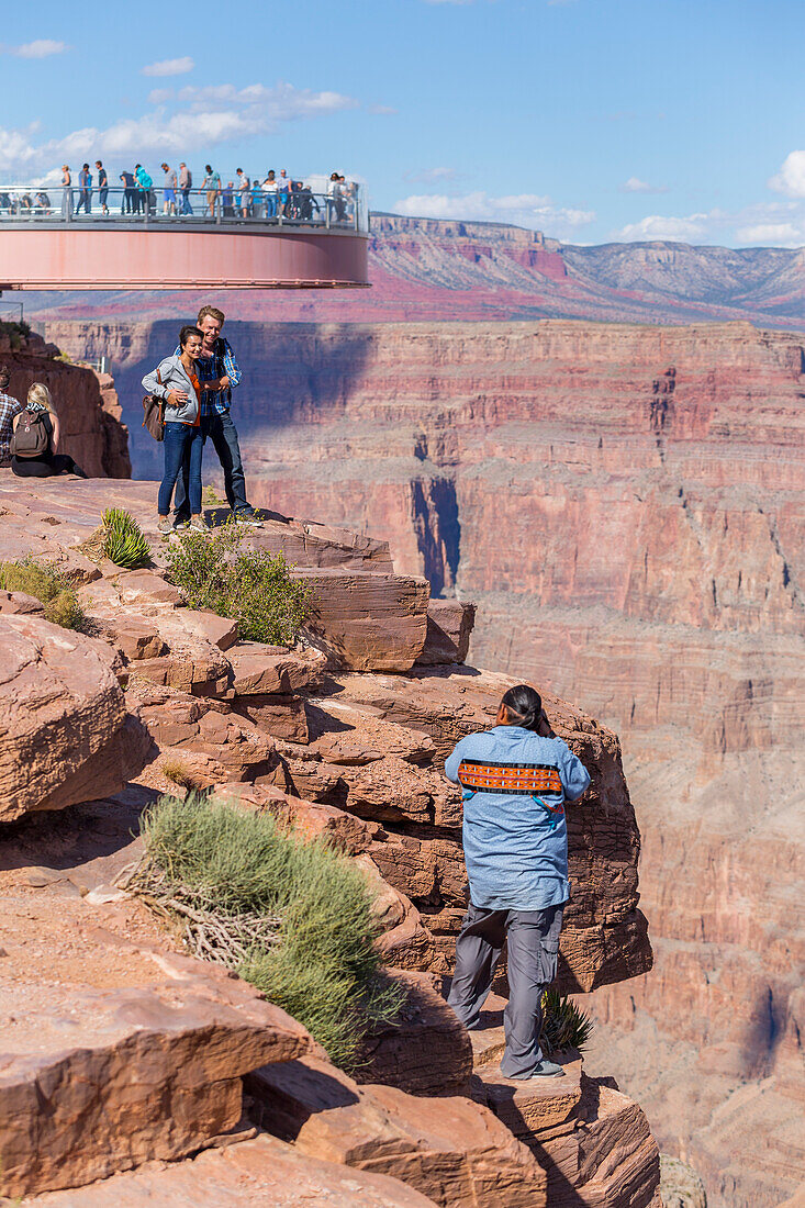 'A native american worker photographs tourists at the Skywalk Viewpoint over the West Grand Canyon natural landscape area in Arizona, a popular tourist attraction operated by the indigenous native American people; Arizona, United States of America'