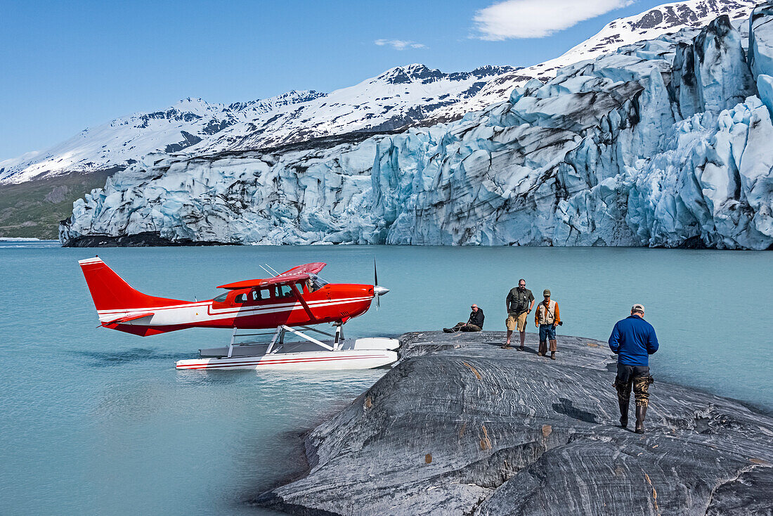 Tourists on a rock outcrop in front of Colony Glacier and Lake George, Southcentral Alaska, USA