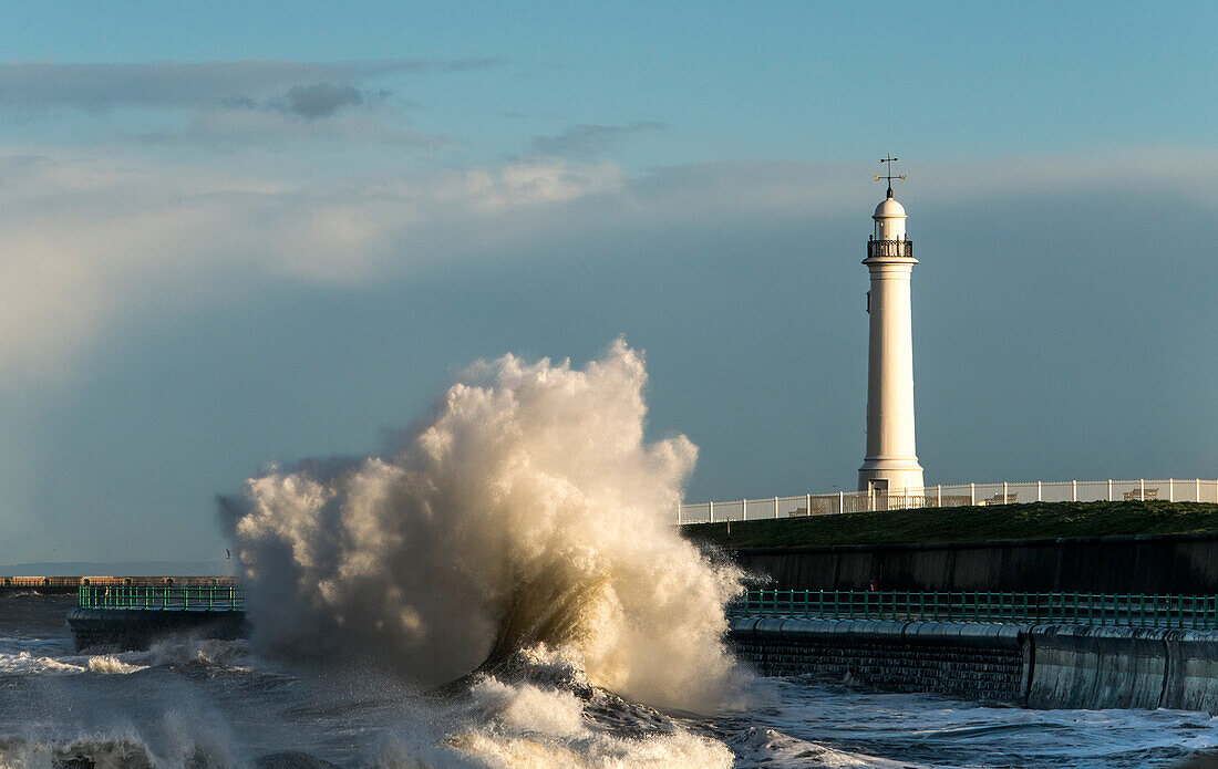 Eine große Welle, die gegen die Wand am Ufer unterhalb eines Leuchtturms stürzt, Sunderland, Tyne und Wear, England