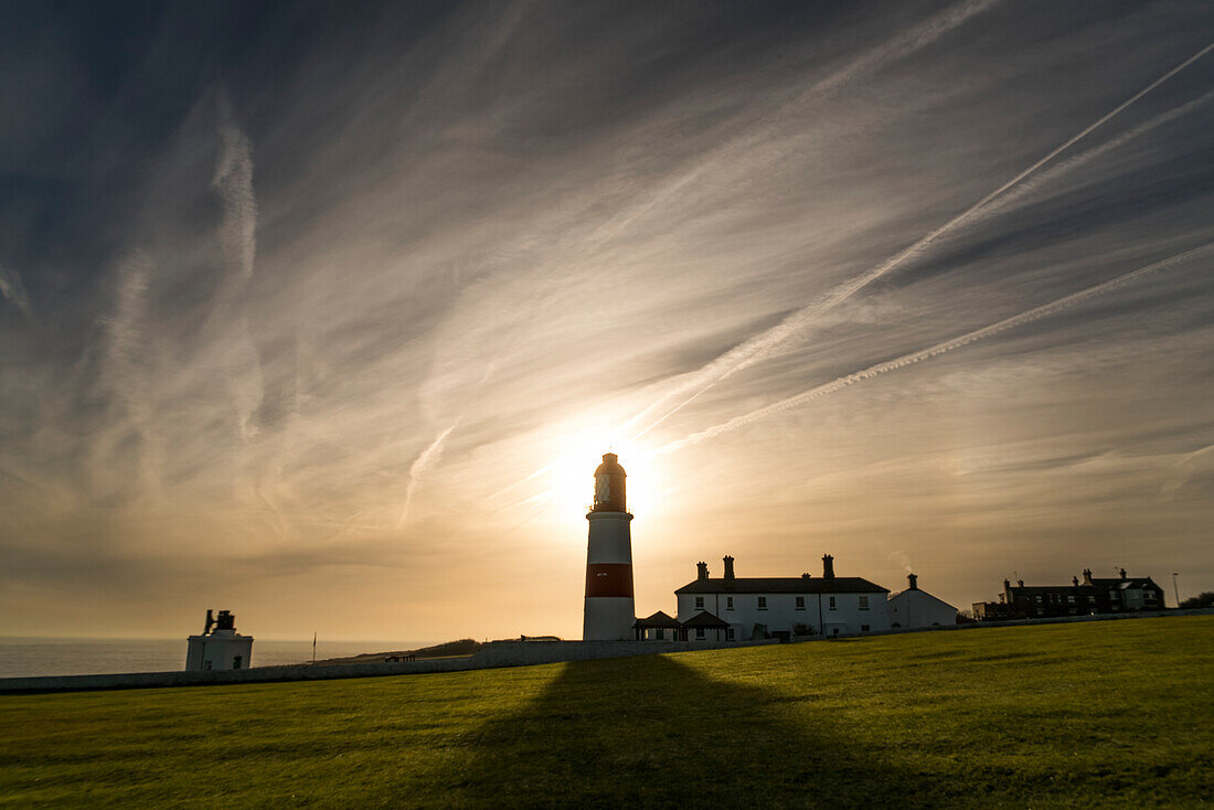Sonnenlicht hinter einem Leuchtturm wirft einen Schatten auf eine Wiese entlang der Küste, South Shields, Tyne und Wear, England