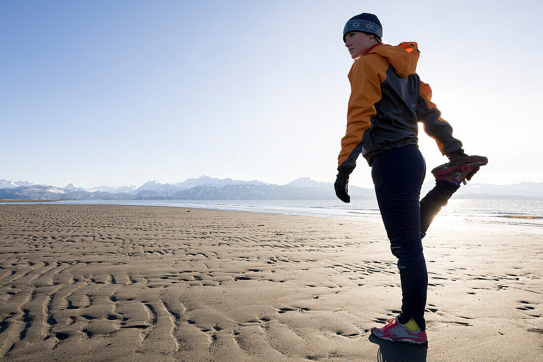 A young woman stretches on the wet beach before running, Homer, Alaska, United States of America