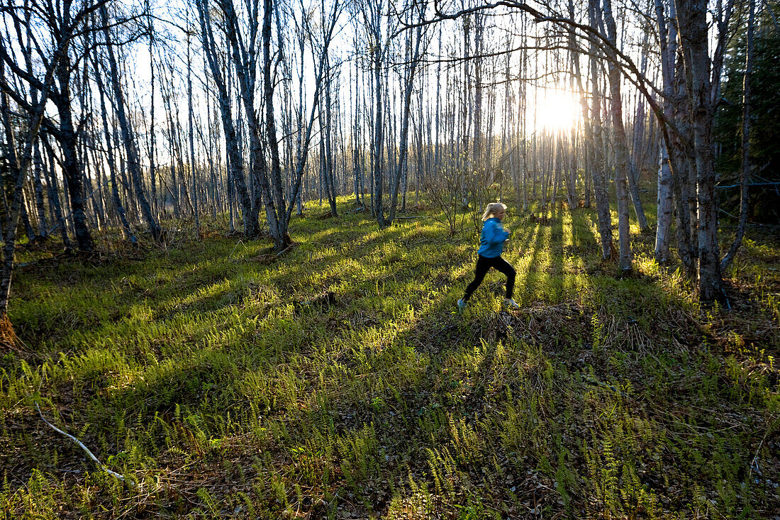 A young woman running across the plants of the forest floor in a forest, Homer, Alaska, United States of America