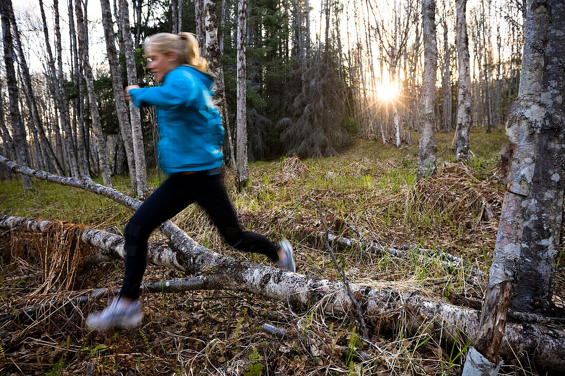 A young woman running over logs on a forest floor in a forest, Homer, Alaska, United States of America