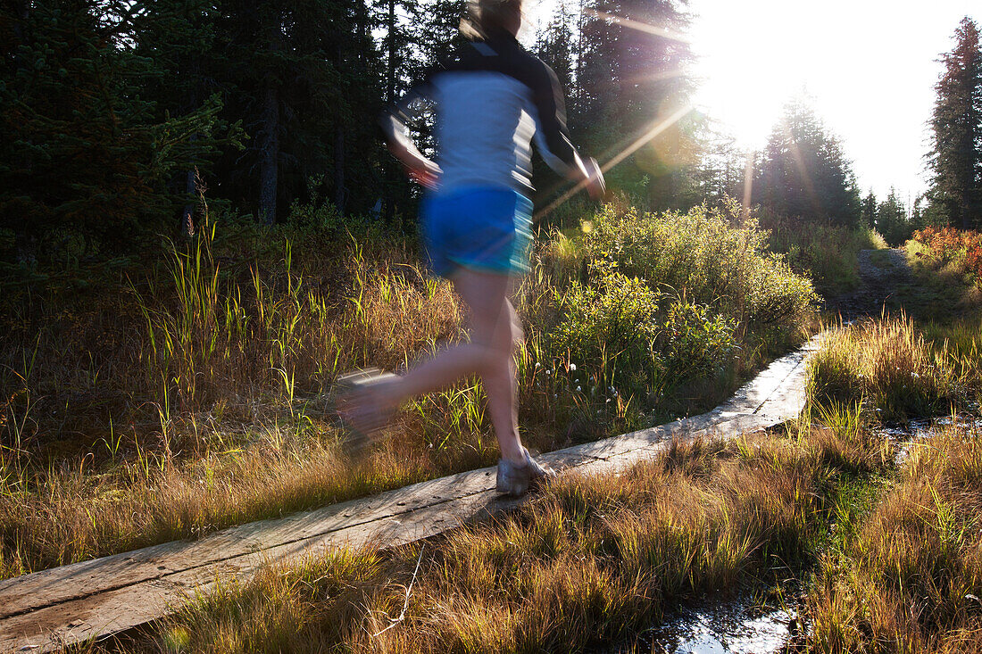 A young woman runs on wooden boards through a forest, Homer, Alaska, United States of America