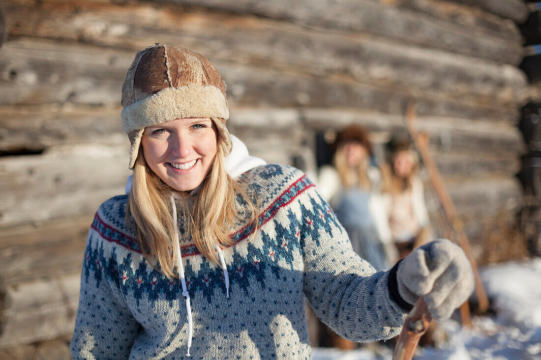 Porträt einer jungen Frau trägt einen Hut und Pullover von einem Blockhaus im Winter, Homer, Alaska, Vereinigte Staaten von Amerika