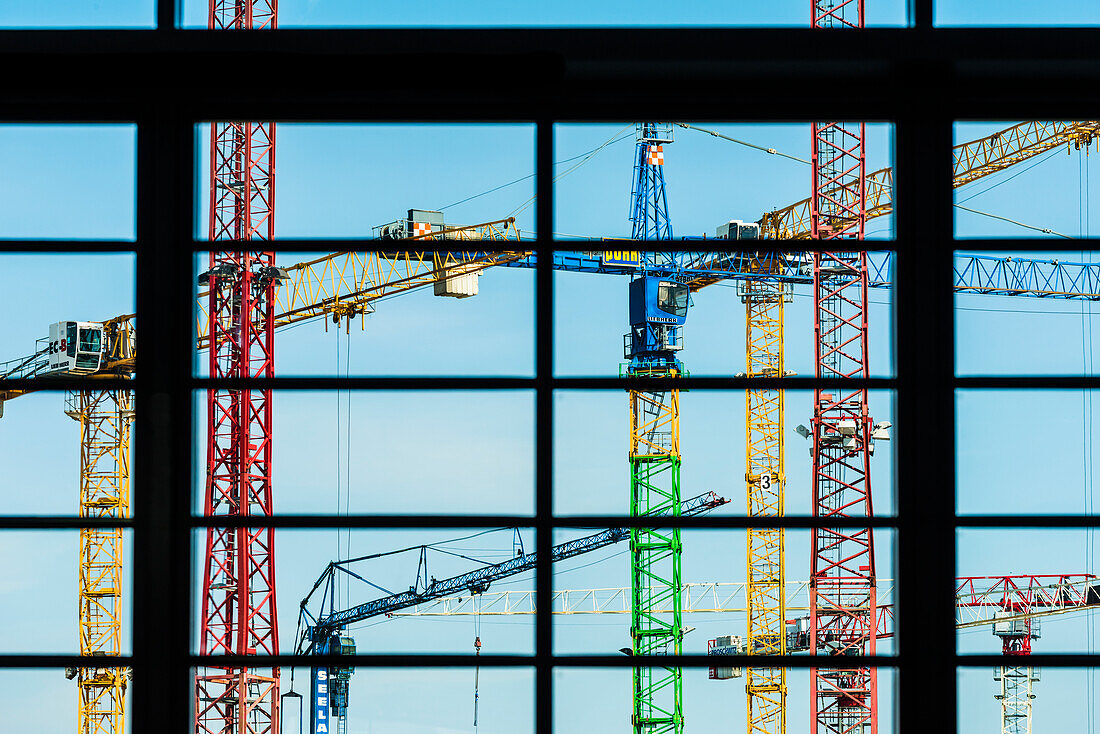 Bunte Baukräne auf einer Großbaustelle durch ein Fenster gesehen, Hamburg, Deutschland