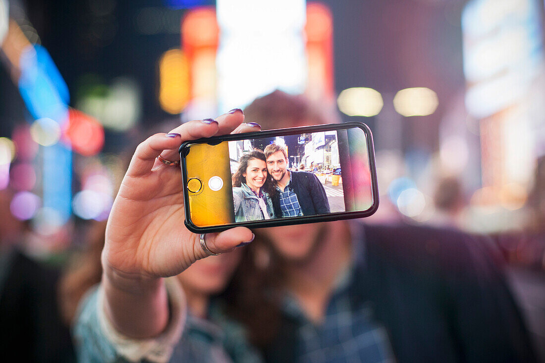 Junges Paar, das selfie in beleuchteter Stadtstraße nimmt