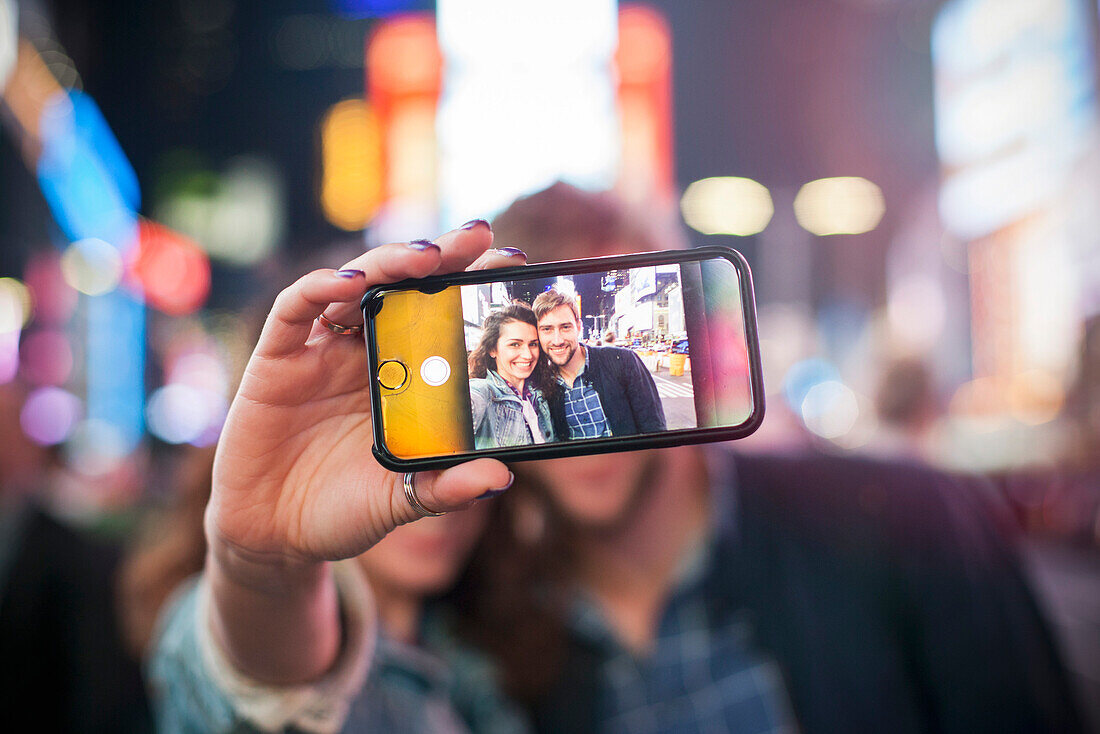 Young couple taking selfie in illuminated city street