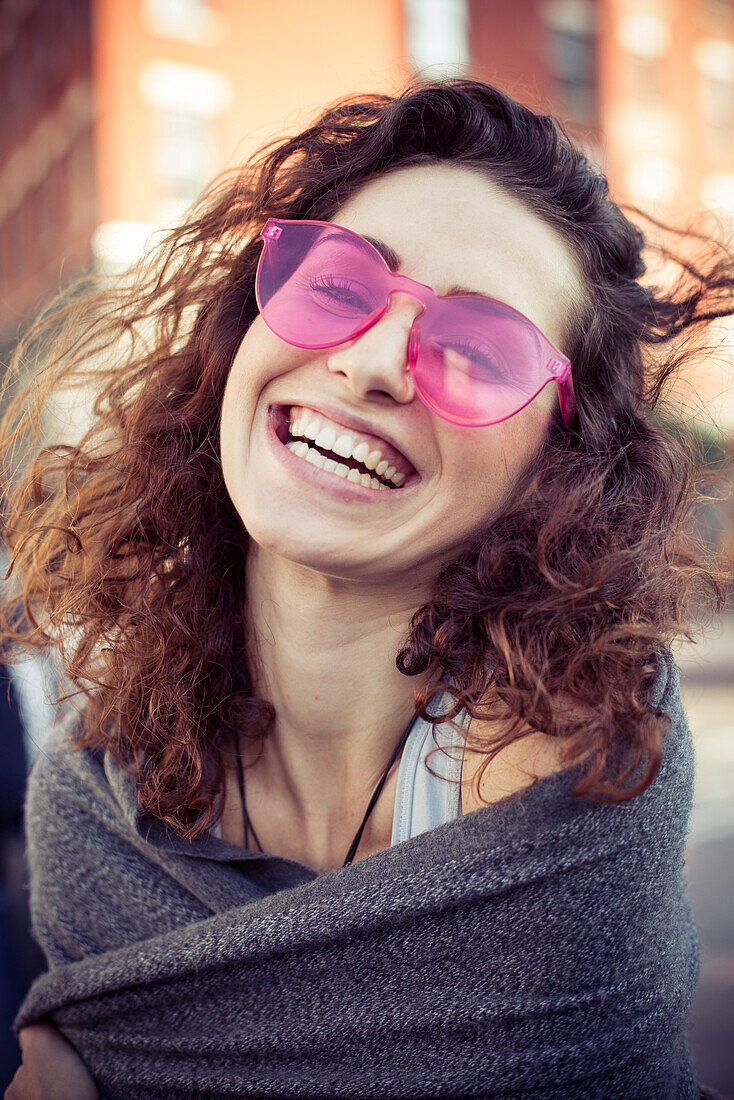 Woman wearing pink sunglasses, laughing, portrait