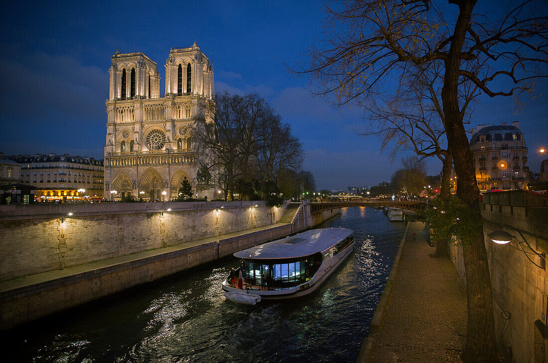 A pleasure boat moves past Notre Dame Cathedral on the Seine River at twilight, Paris, France
