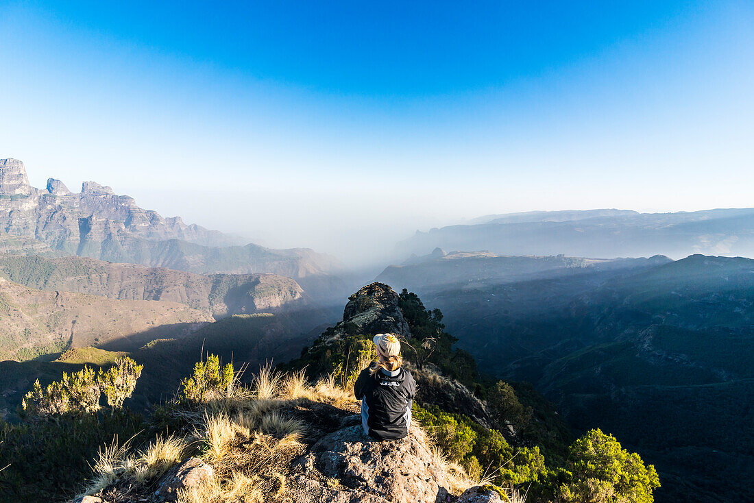 Woman enjoying the early morning sun on the cliffs, Simien Mountains National Park, UNESCO World Heritage Site, Debarq, Ethiopia, Africa