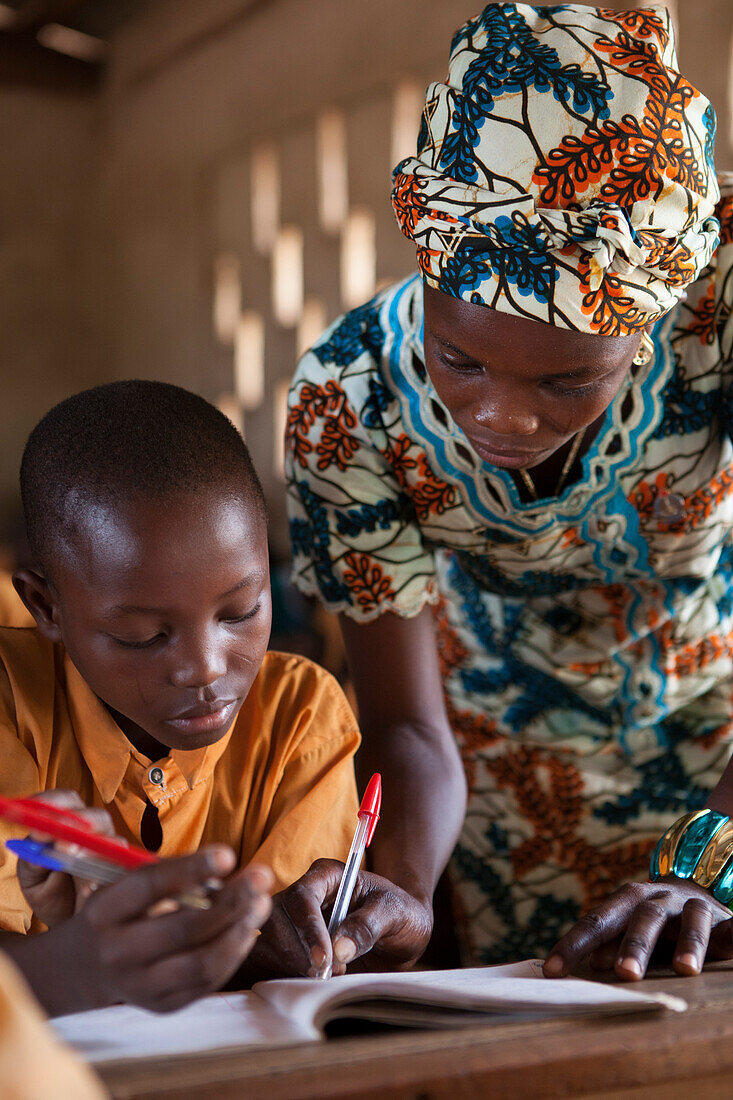 Ein Lehrer hilft einem jungen Schüler an einer Schule, Ghana, Westafrika, Afrika