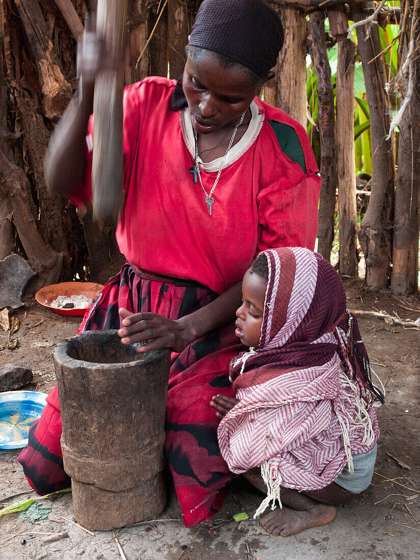 A woman uses a traditional wooden pestle and mortar to grind freshly roasted coffee beans, Ethiopia, Africa