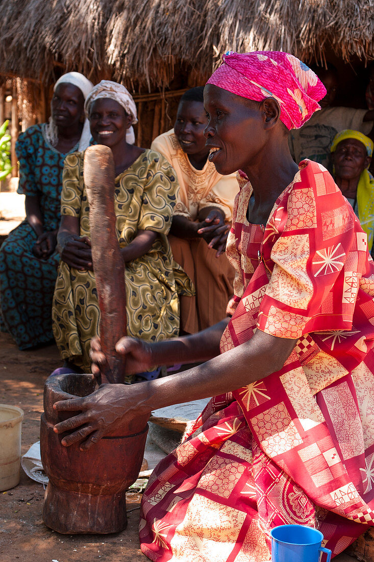 Eine Frau stampft Hirse mit einem traditionellen hölzernen Stößel und Mörtel an ihrer Heimatverbindung, Uganda, Afrika