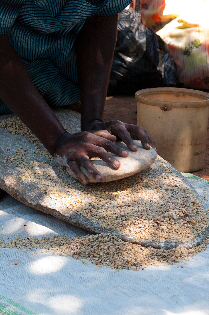 A woman using two stones to grind grain in to flour, Uganda, Africa