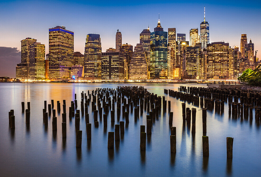 Lower Manhattan skyline, New York skyline, exposed wooden pier stumps, at night, East River, New York, United States of America, North America