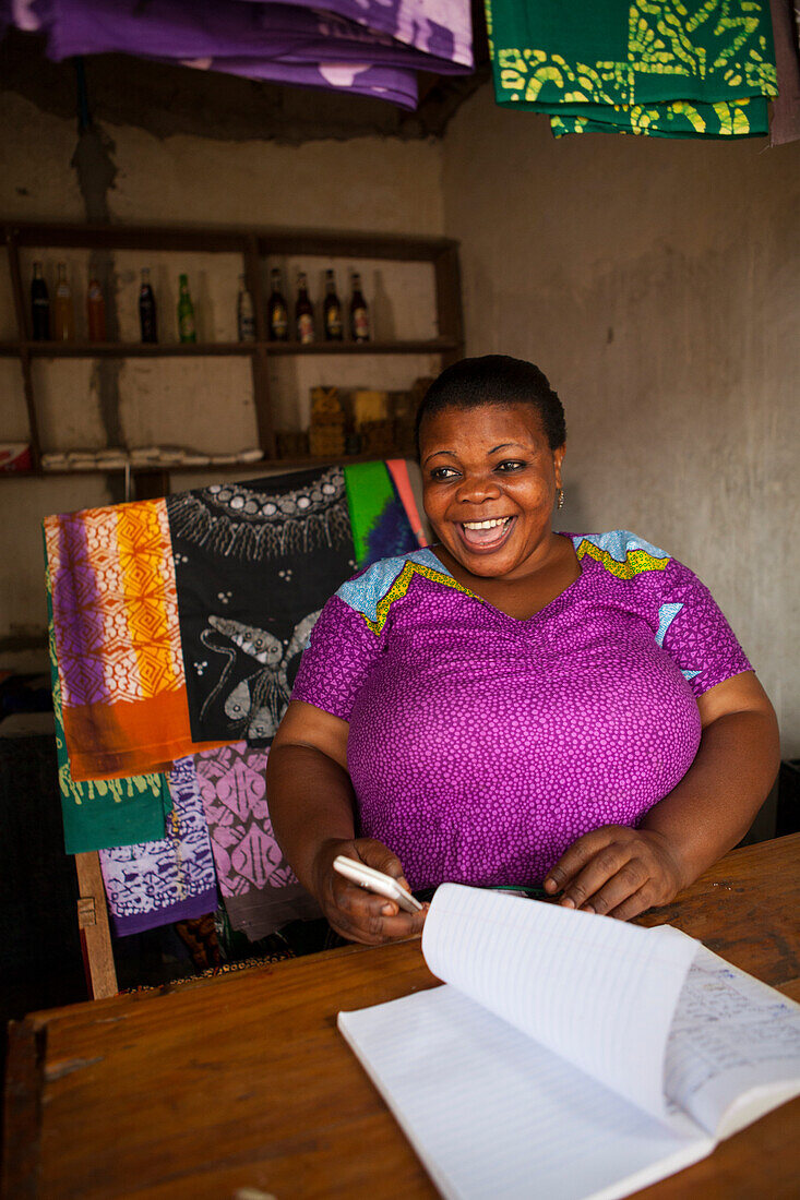 Eine Frau lächelt hinter dem Ladentisch ihres Ladens, Tansania, Ostafrika, Afrika