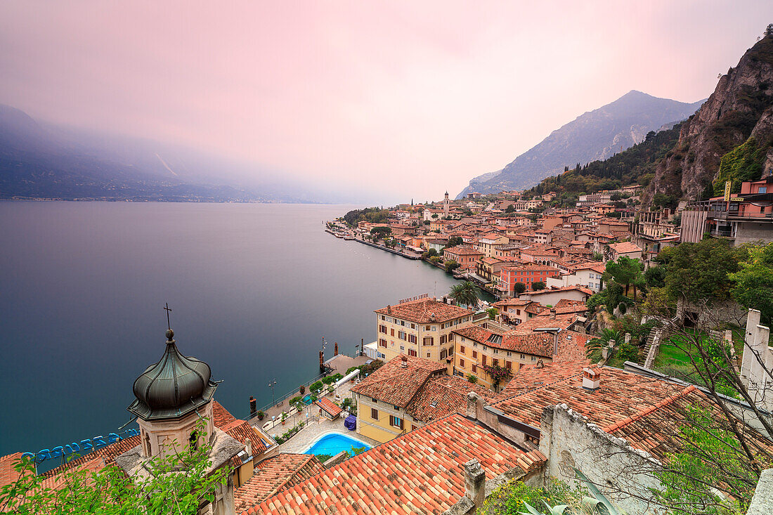 Pink sunrise lights up Lake Garda and the typical town of Limone Sul Garda, province of Brescia, Italian Lakes, Lombardy, Italy, Europe