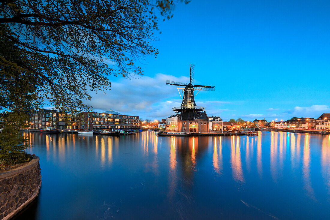 Dusk lights on the Windmill De Adriaan reflected in the River Spaarne, Haarlem, North Holland, The Netherlands, Europe