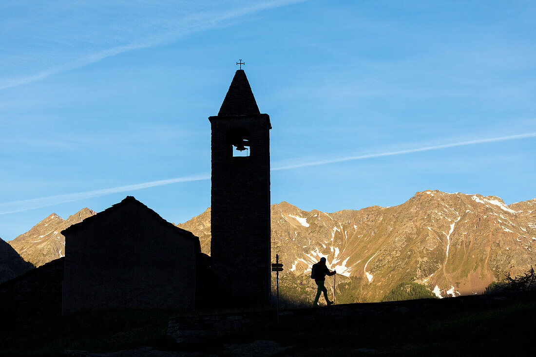 Silhouette of hiker at the old church at dawn, San Romerio Alp, Brusio, Canton of Graubünden, Poschiavo valley, Switzerland