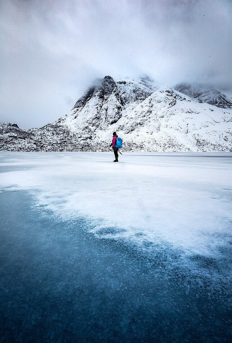 Ein Fotograf zu Fuß auf einem zugefrorenen See, Lofoten Island, Norwegen