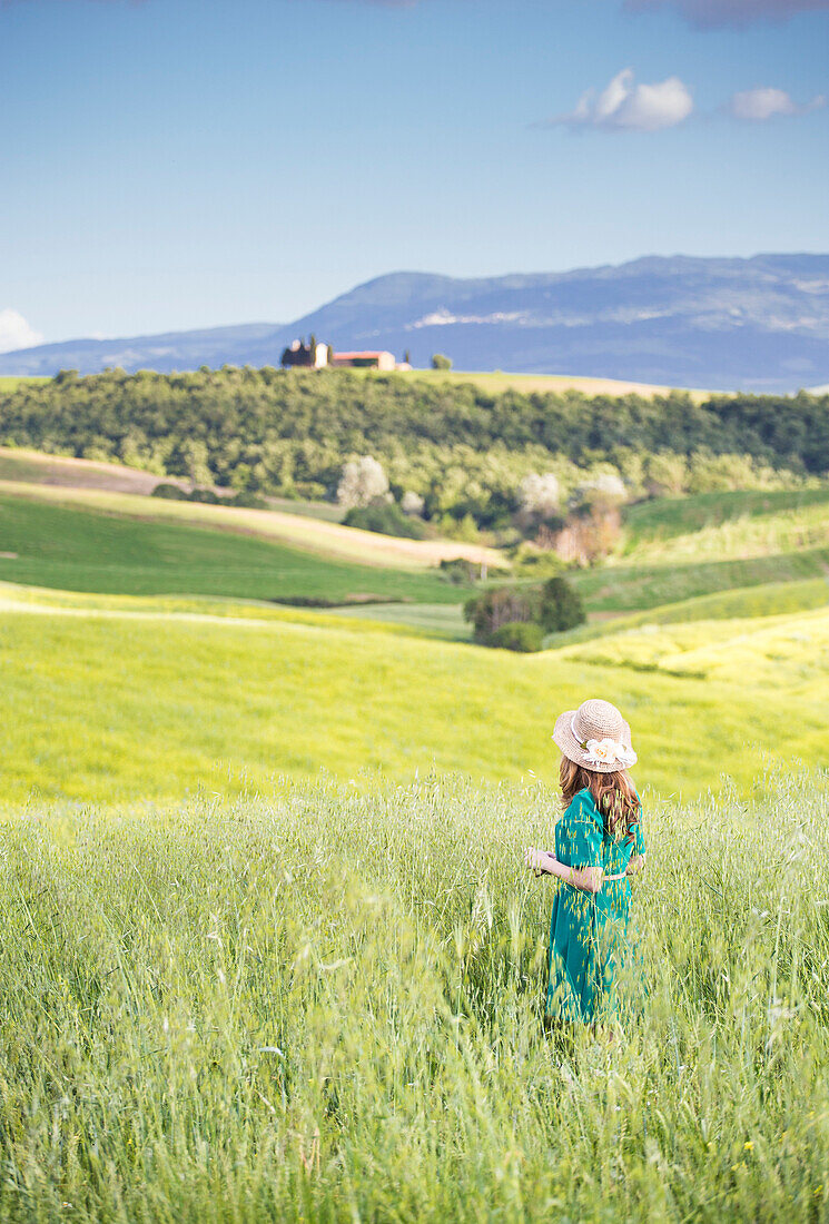 Ein Mädchen in einem grünen Kleid durch die goldenen Felder der Toskana, Val d'Orcia, Provinz Siena, Toskana, Italien