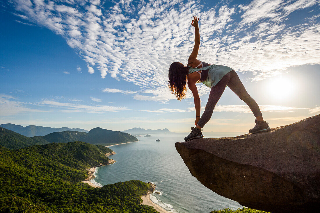 Woman in yoga posture on the edge of the mountain in Pedra do TelÃ©grafo, Barra de Guaratiba, west side of Rio de Janeiro, Brazil