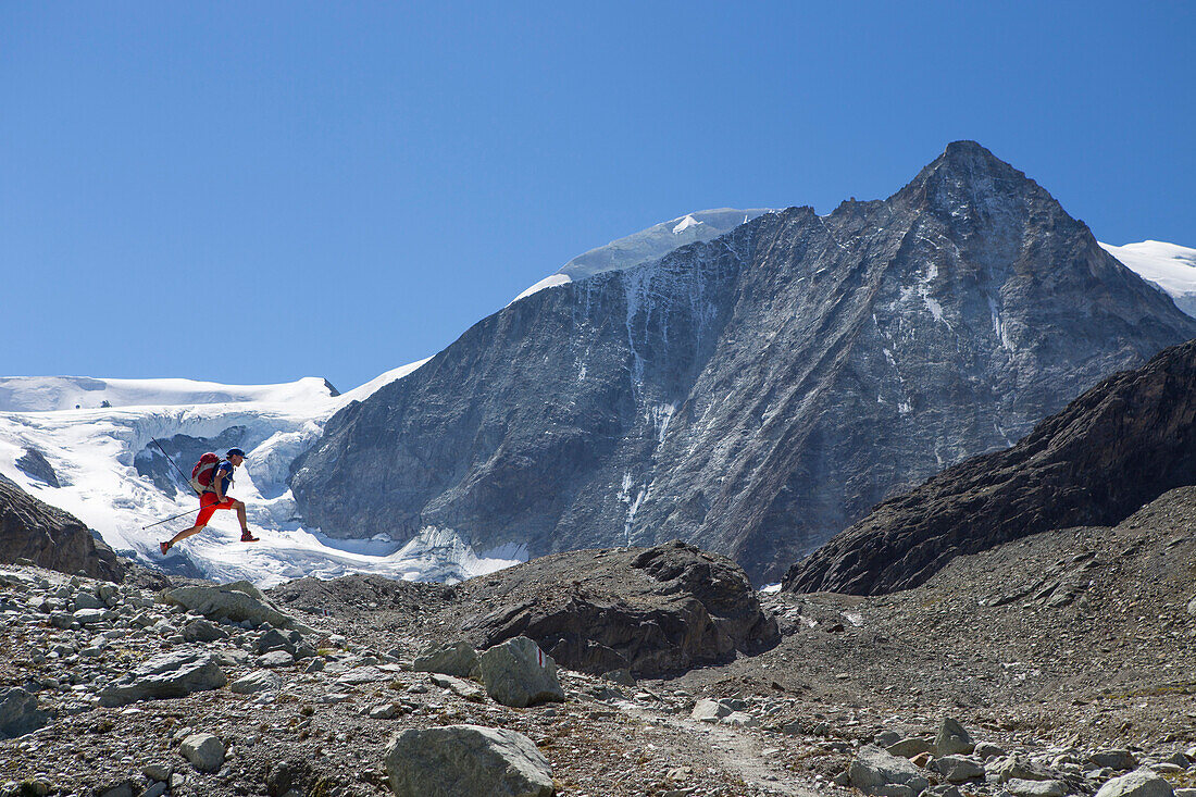 A male hiker is happily jumping in the air, in front of the Mont Blanc de Cheilon, a mountain at the end of the Val d'HÃ©rÃ©mence in the Swiss region of Valais. This is halfway the Haute Route, a popular alpine hike through France and Switzerland.