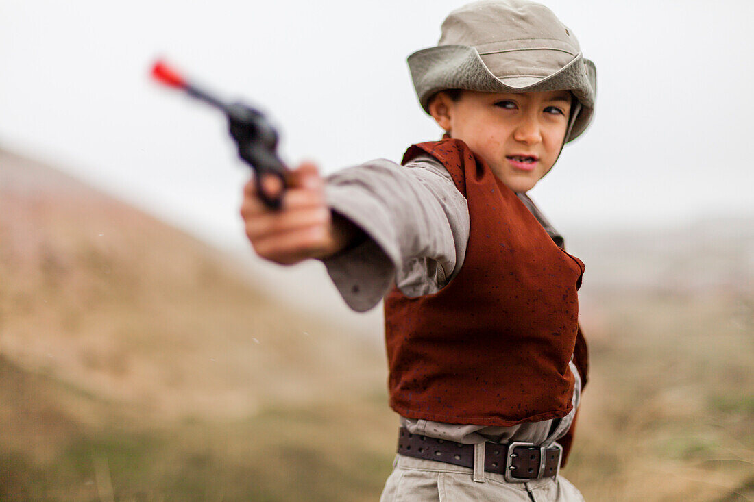 'Ein 6-jähriger japanisch-amerikanischer Junge, der als Entdecker mit Hut und Weste verkleidet ist, benutzt seine Pistole (sechs Schützen), als er ''schlechte Jungs'' bekommt? wie er in Badlands National Park, South Dakota erforscht.'