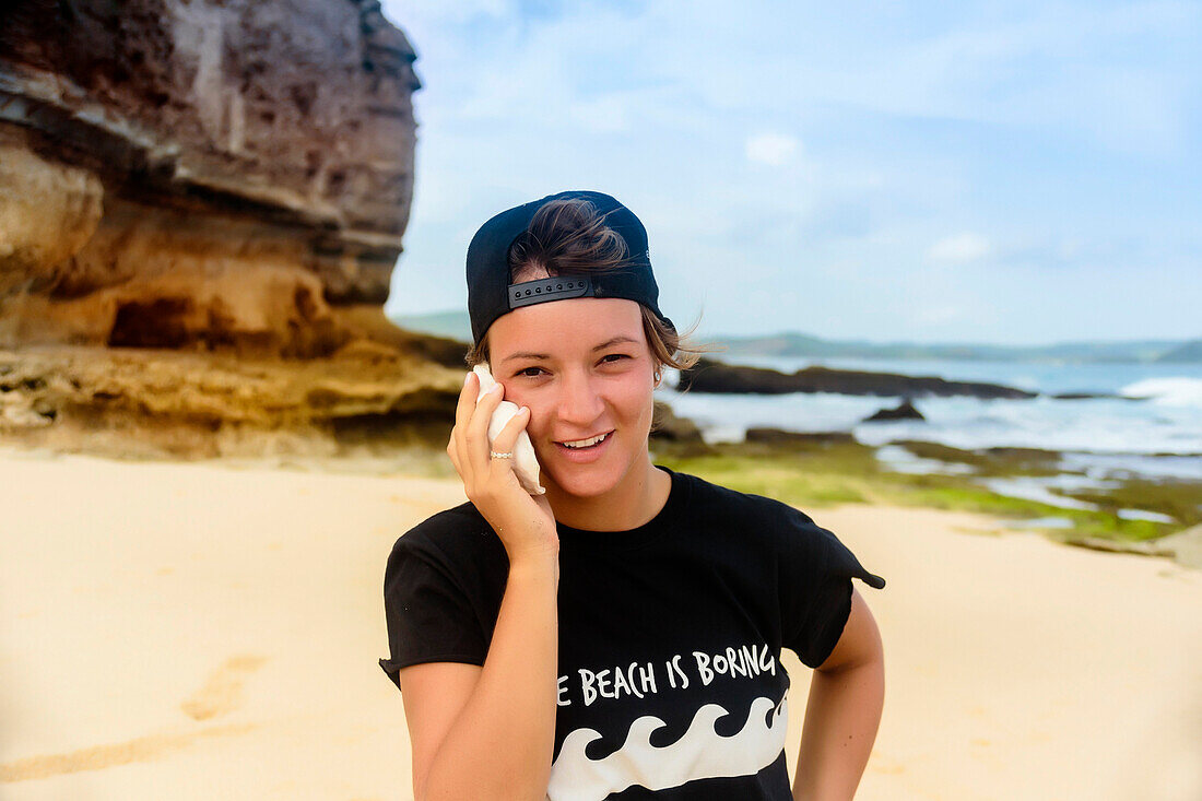 Young woman holding seashell against ear on sandy beach