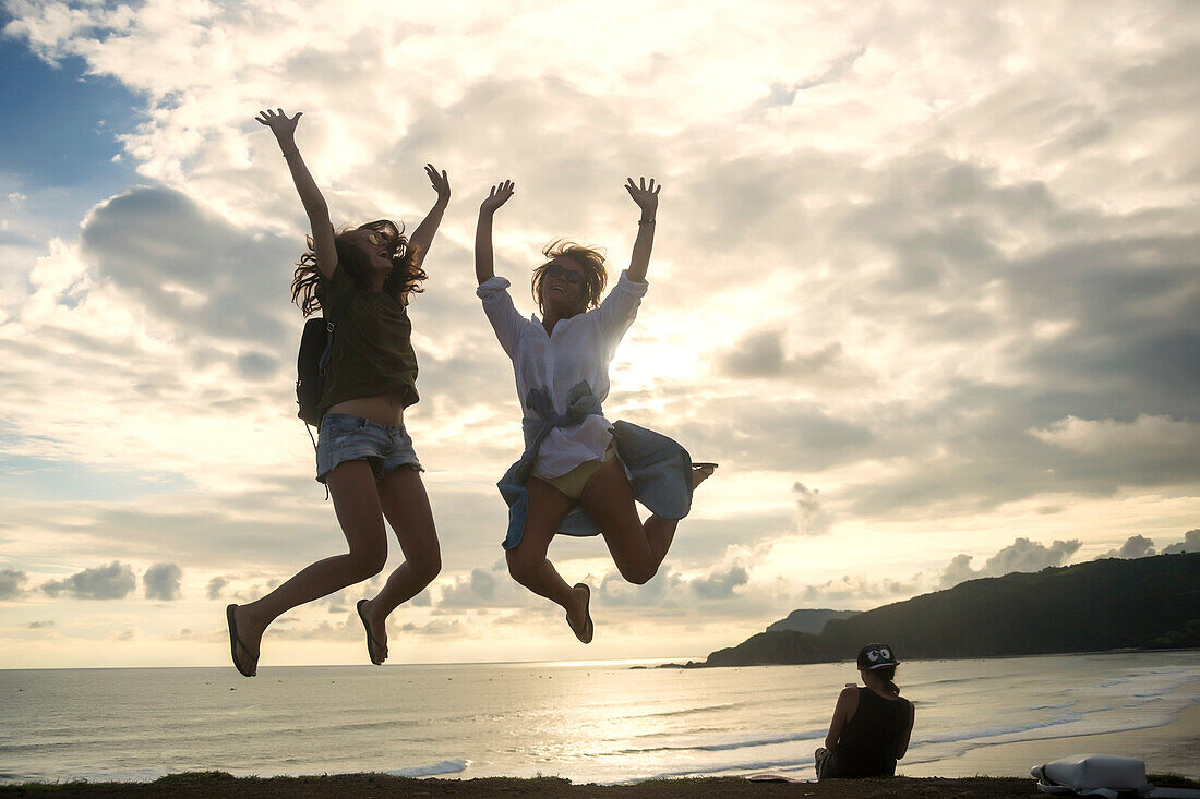 Young women jumping with arms raised on coastline
