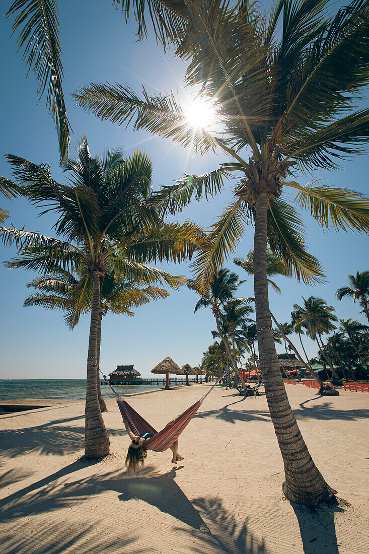 Eine junge Frau liegt in einer Hängematte zwischen Palmen am Strand