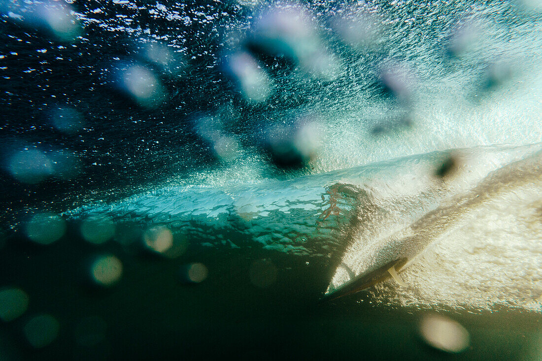Unterwassersicht einer Welle und eines Surfers auf einer Sonnenaufgangssitzung