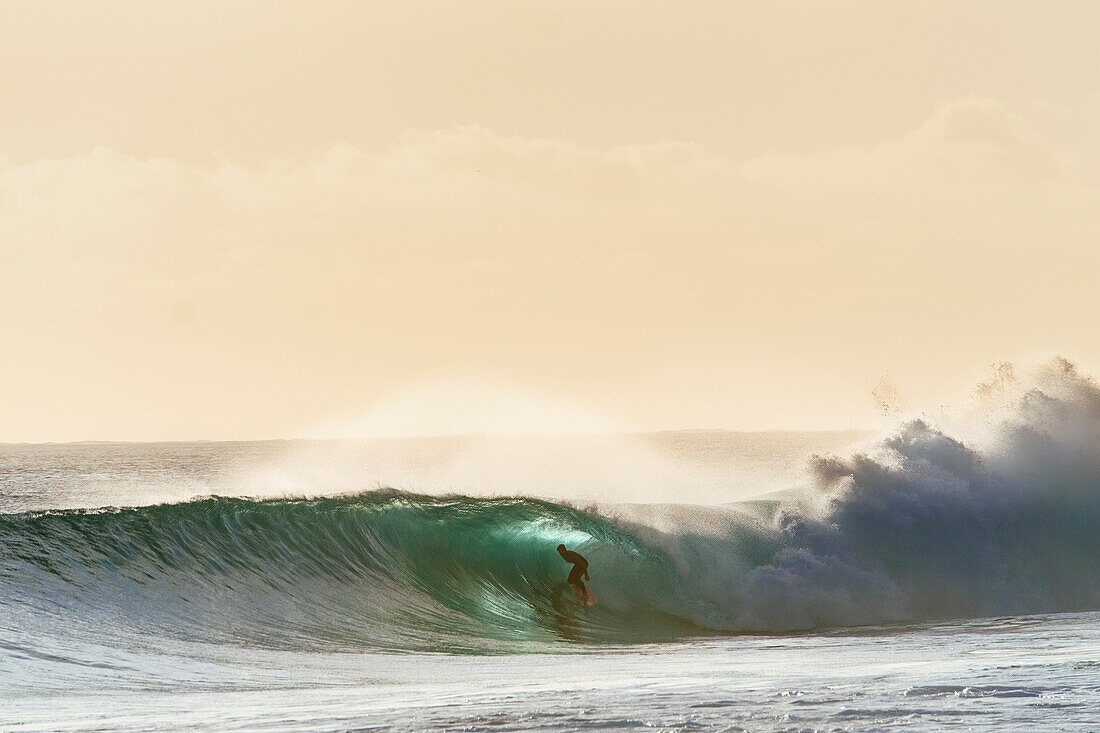 Ein Surfer wird vor dem Sonnenuntergang barreled