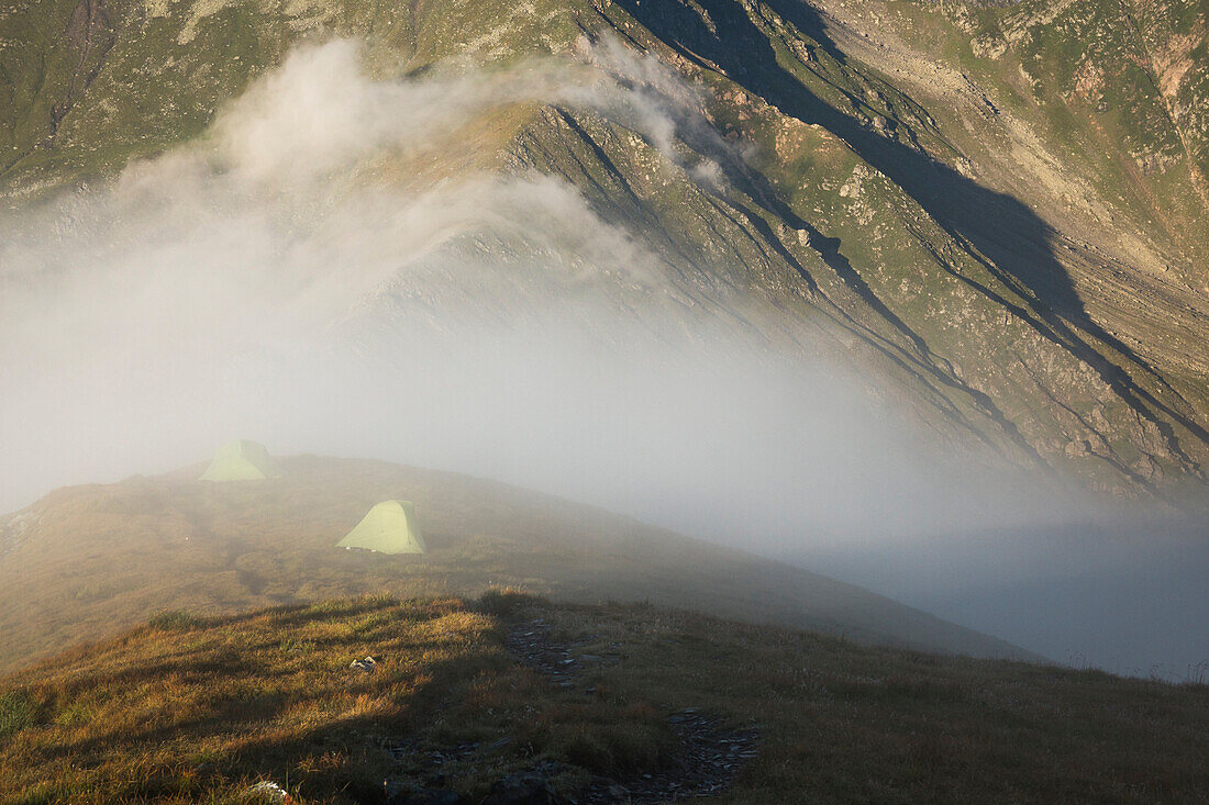 Zelte in alpiner Umgebung von Nebel bei Sonnenaufgang verschlungen