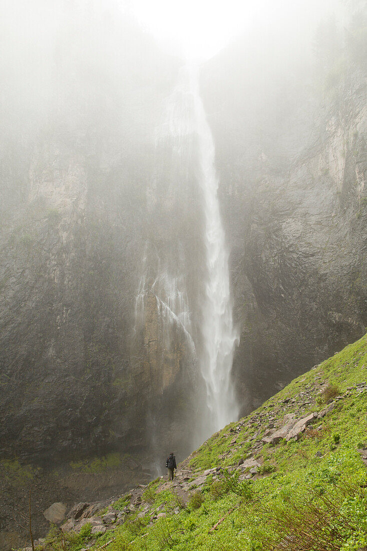 A hiker walks past Comet Falls in Mount Rainier on a cloudy rainy day.