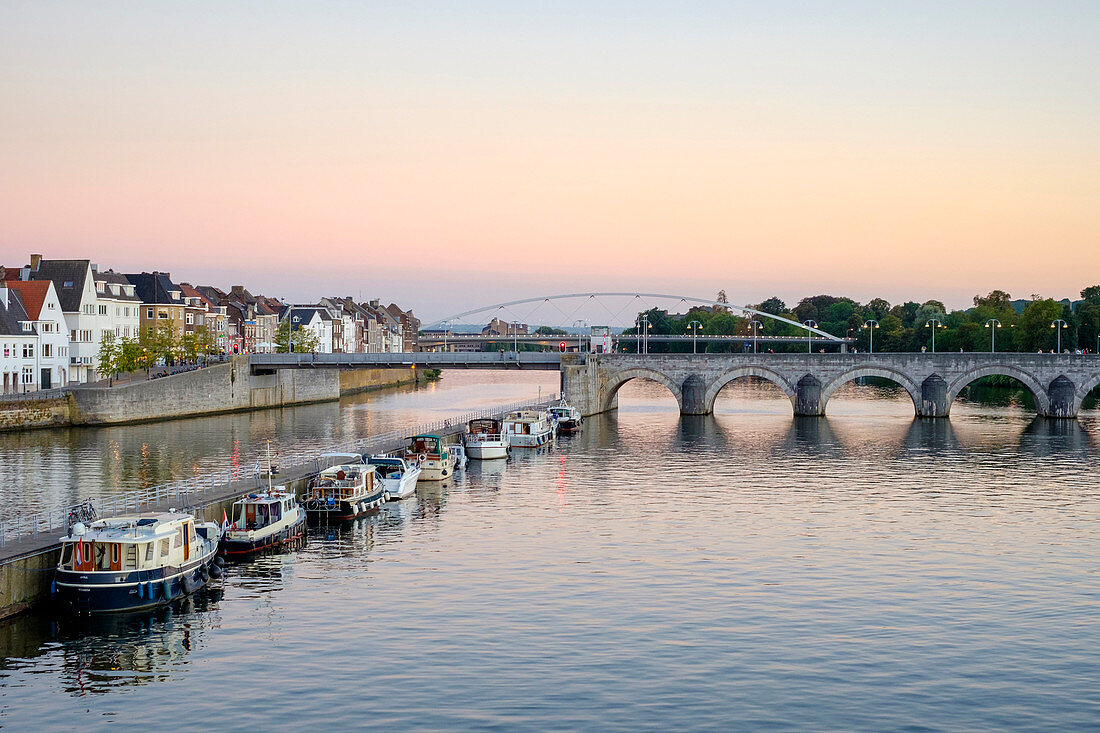 Photograph of Meuse River with bridge, boats and buildings on bank, Maastricht, Limburg, Netherlands