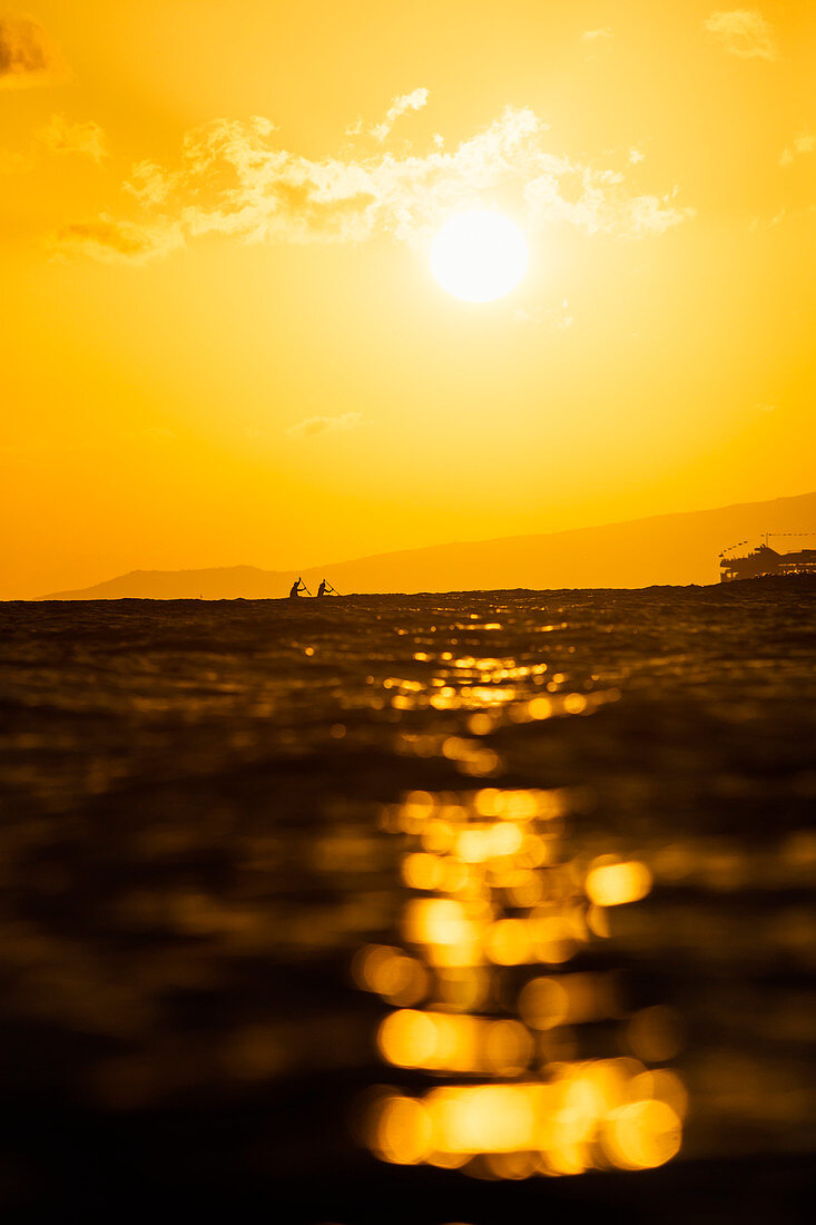 Two men paddling in sea at sunset, Kaimana Beach, Honolulu, Hawaii, USA