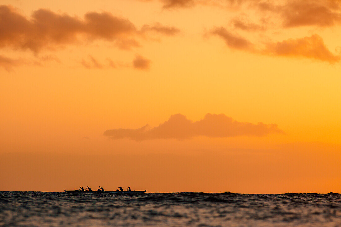 Group of men paddling in sea at sunset, Kaimana Beach, Honolulu, Hawaii, USA