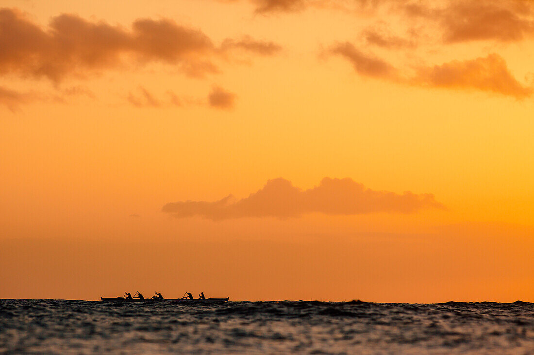 Gruppe von Männern paddeln im Meer bei Sonnenuntergang, Kaimana Beach, Honolulu, Hawaii, USA