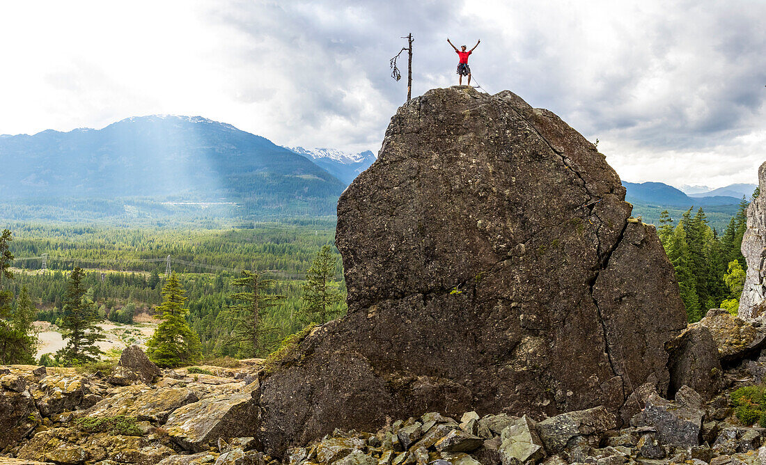 Rock climber standing in victory pose on top of rock, Whistler, British Columbia, Canada