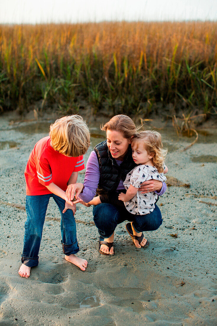 Frau kniet mit ihrer Tochter in Arm im Sumpf, Wrightsville Beach, North Carolina, USA