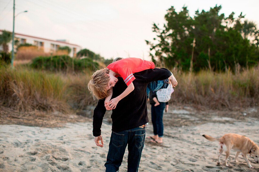 Ein Mann trägt seinen Sohn über seine Schulter in einem Sumpf in Wrightsville Beach, NC.