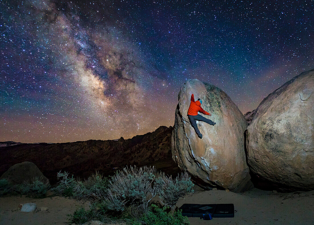 Milky way on dark sky over person climbing on rock, California, USA