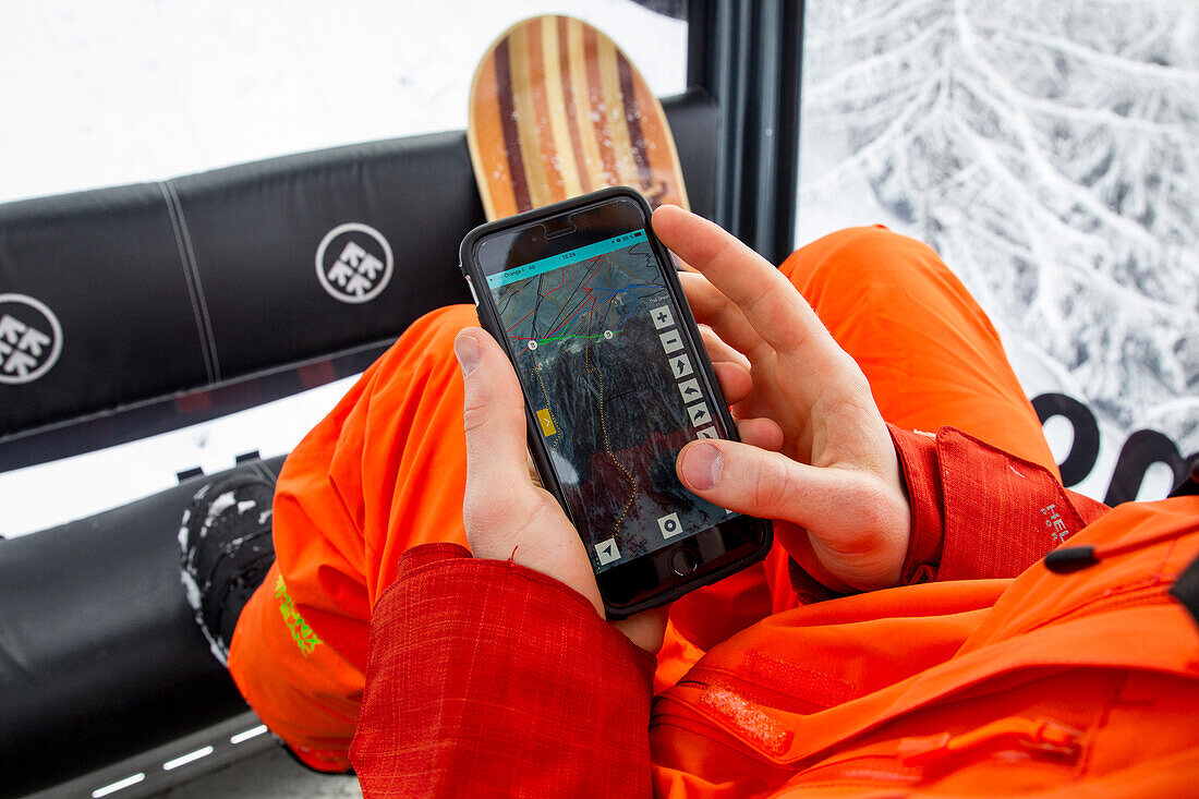 Snowboarder using a phone to check the free ride lines in the lift