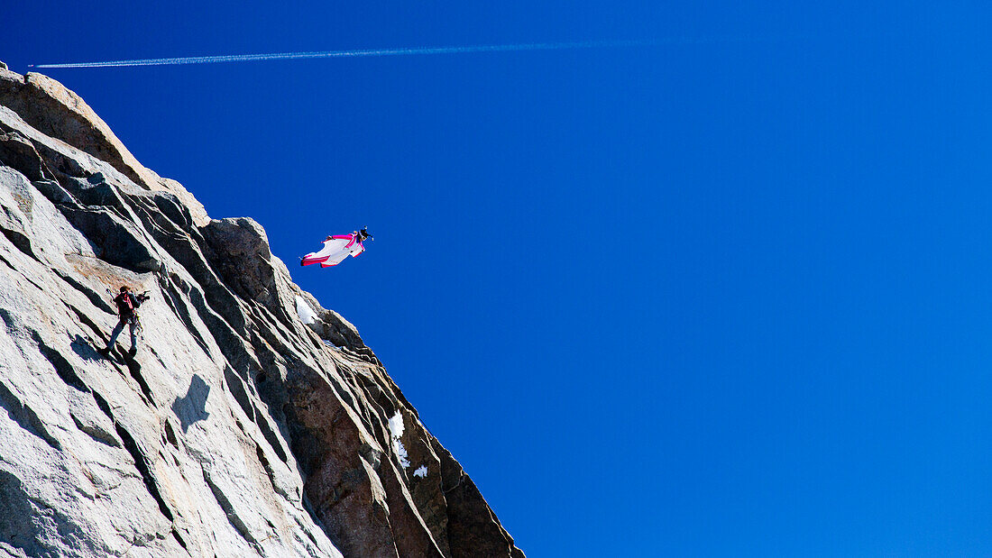 Eine Person springt von einer Klippe in einem Wingsuit in den Alpen