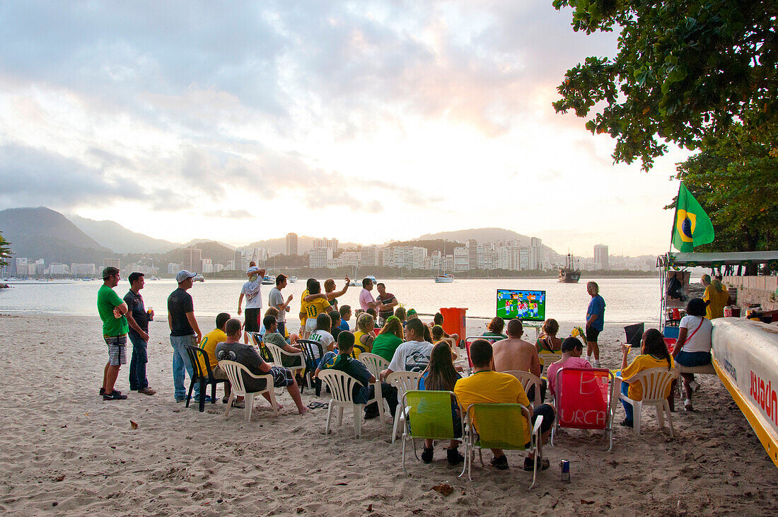 Eine Gruppe von lokalen Fußballfans beobachten ein Fußballspiel im Fernsehen am Strand