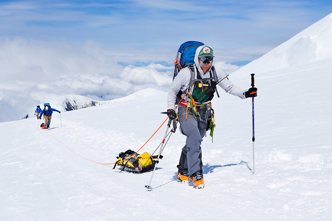 Ski-Bergsteiger und Rangers auf dem Weg zu 14.000 Meter auf Denali in Alaska. Kletterer auf dem höchsten Gipfel Nordamerikas tragen ihre Lasten in Rucksäcken und auf Schlitten.